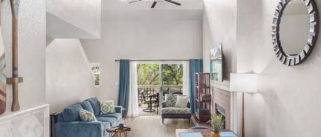 A spacious living area with a ceiling fan, a dining table with blue placemats, and a view through a glass door to an outdoor patio.