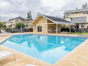 A rectangular swimming pool with clear blue water, surrounded by a tiled deck. There are lounge chairs and a covered seating area with tables. - Waikoloa Hills “Blue Honu Escape” 2br condo getaway in Paradise Pool Golfing (Waikoloa Village)
