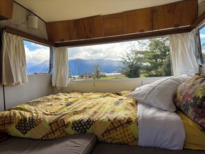 A bed with a patterned bedspread and pillows, a window with curtains, and a view of mountains.