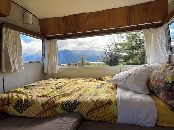 A bed with a patterned bedspread and pillows, a window with curtains, and a view of mountains.