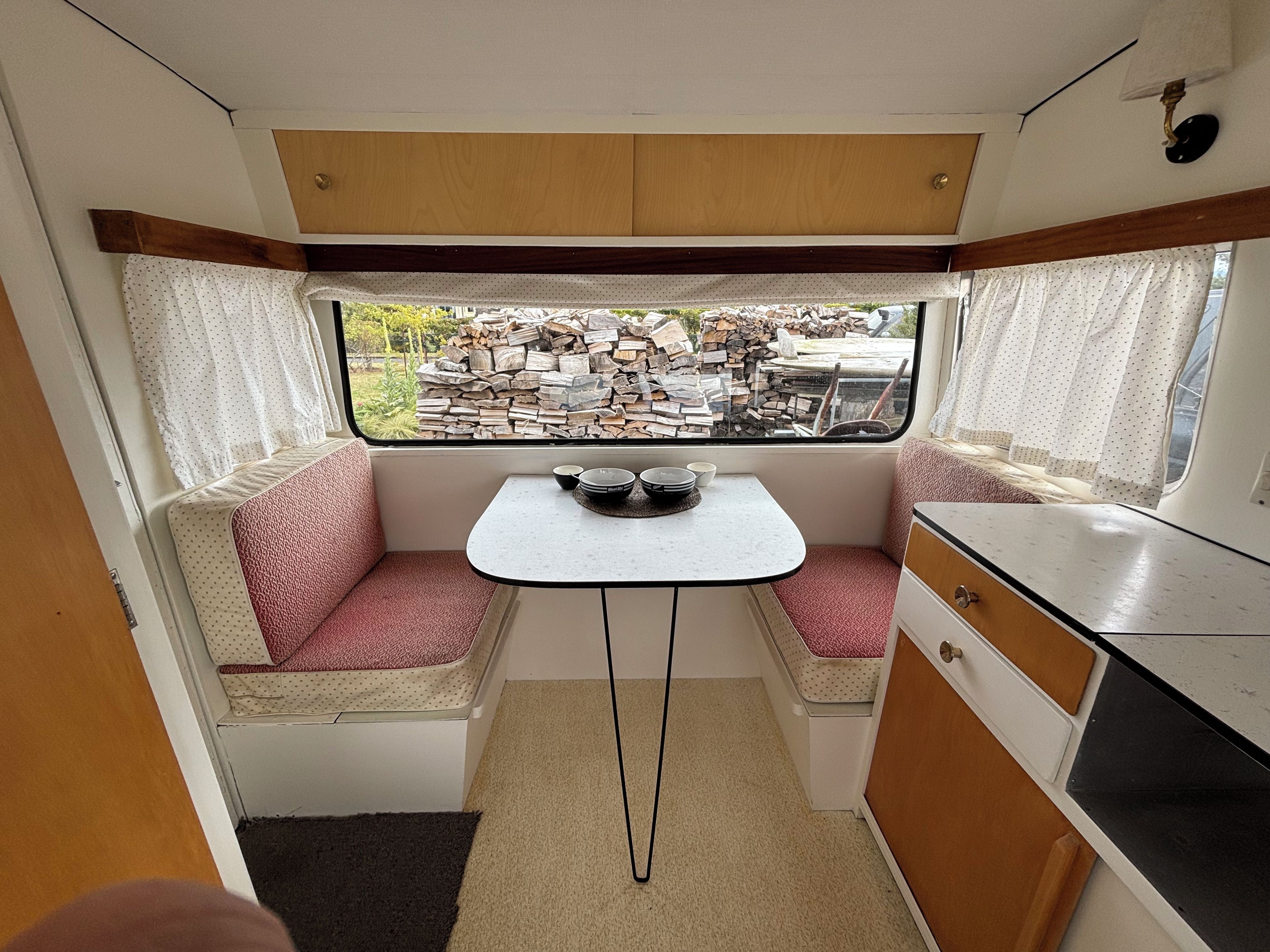 A compact kitchenette with a small dining table, two cushioned seating areas, and a window with a view of an outdoor area.