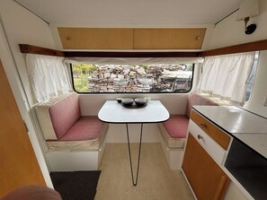 A compact kitchenette with a small dining table, two cushioned seating areas, and a window with a view of an outdoor area. - The Stoney Shore - boutique lakeside camp. Breathtaking lake mountain views (Te Anau)
