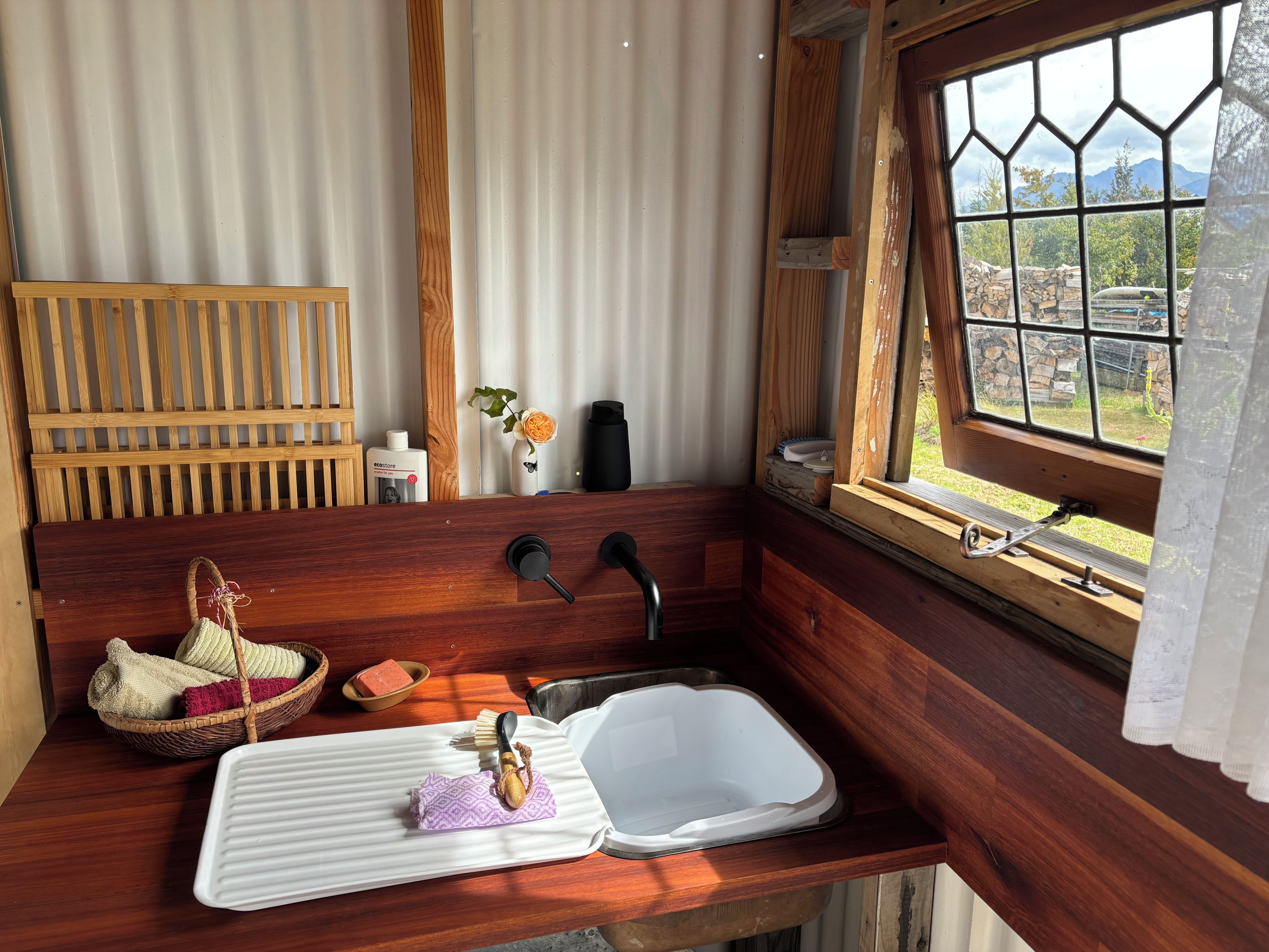 A wooden cabin interior with a wooden bench, a sink, a window with a view of the outdoors, and a basket with towels.