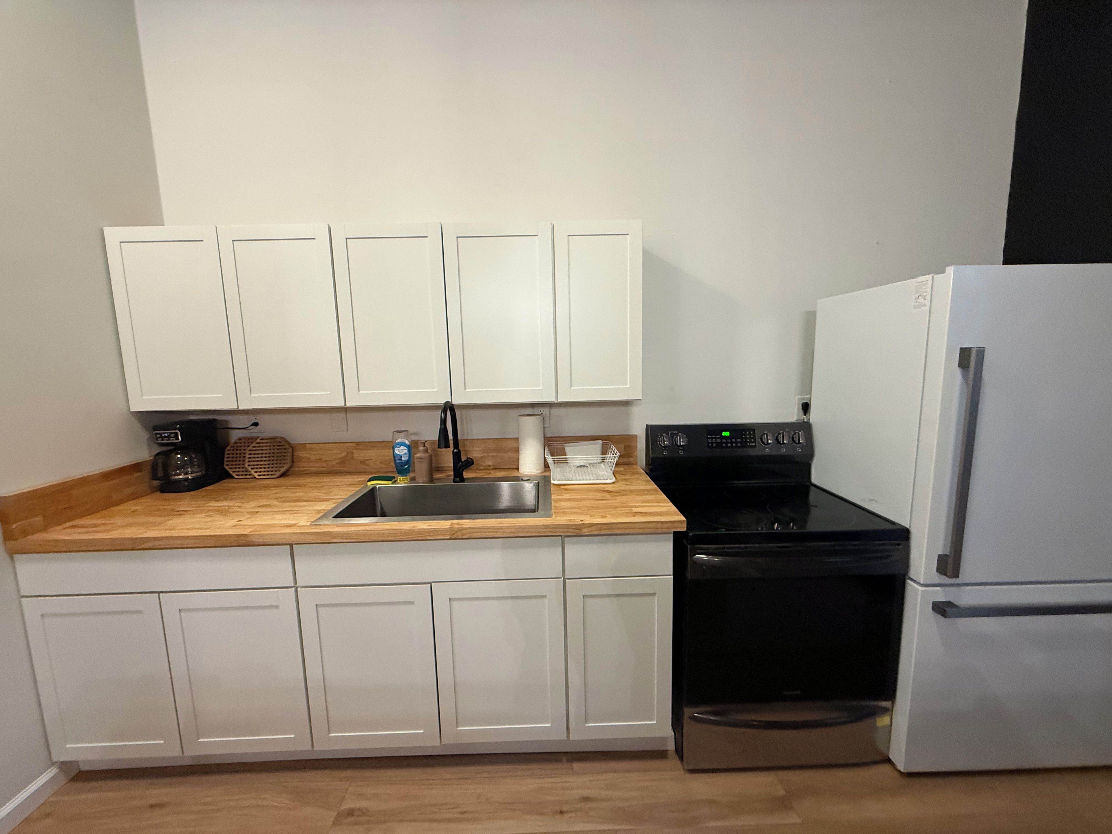A kitchen with white cabinets, a stainless steel sink, a black stove, and a white refrigerator.