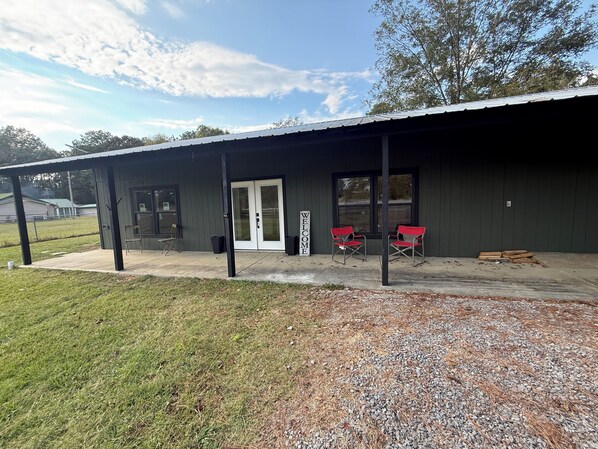A building with a covered porch, a door, and two red chairs.