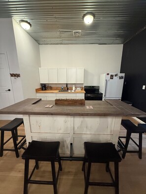 Una cocina con armarios blancos, una encimera de madera, un refrigerador y dos taburetes de bar.