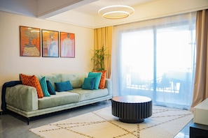 A modern living room with a sofa, cushions, a round table, and artwork on the wall. - Stylish 1 Bedroom Retreat, with a Pool, Gym and Close to the Airport (Nairobi)