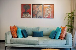 Un salon avec un canapé, trois œuvres d’art encadrées et une plante en pot.