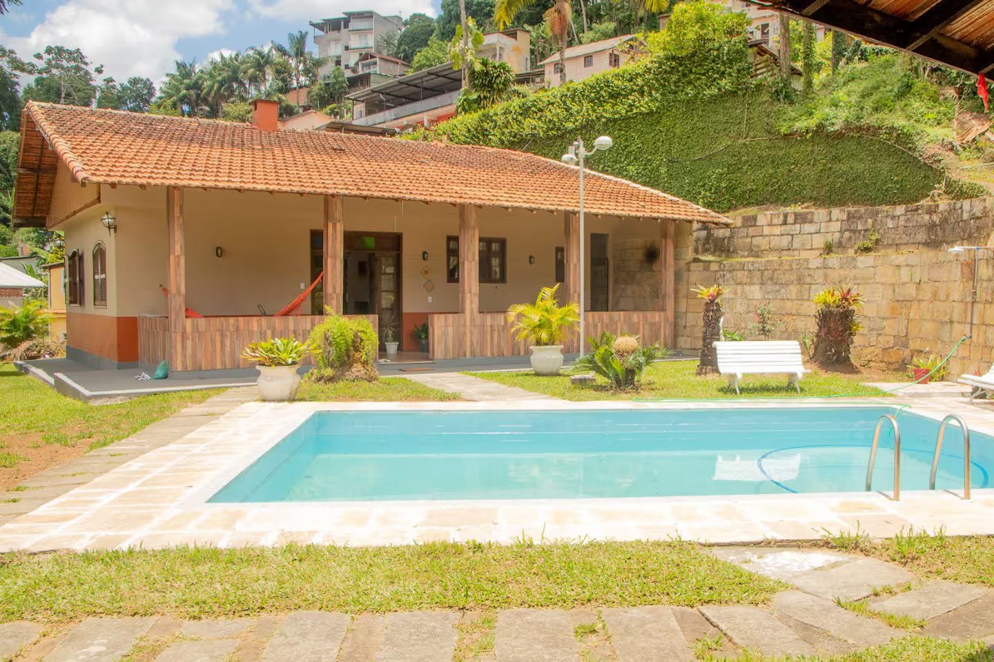 A house with a swimming pool, a covered porch, and a garden with various plants.