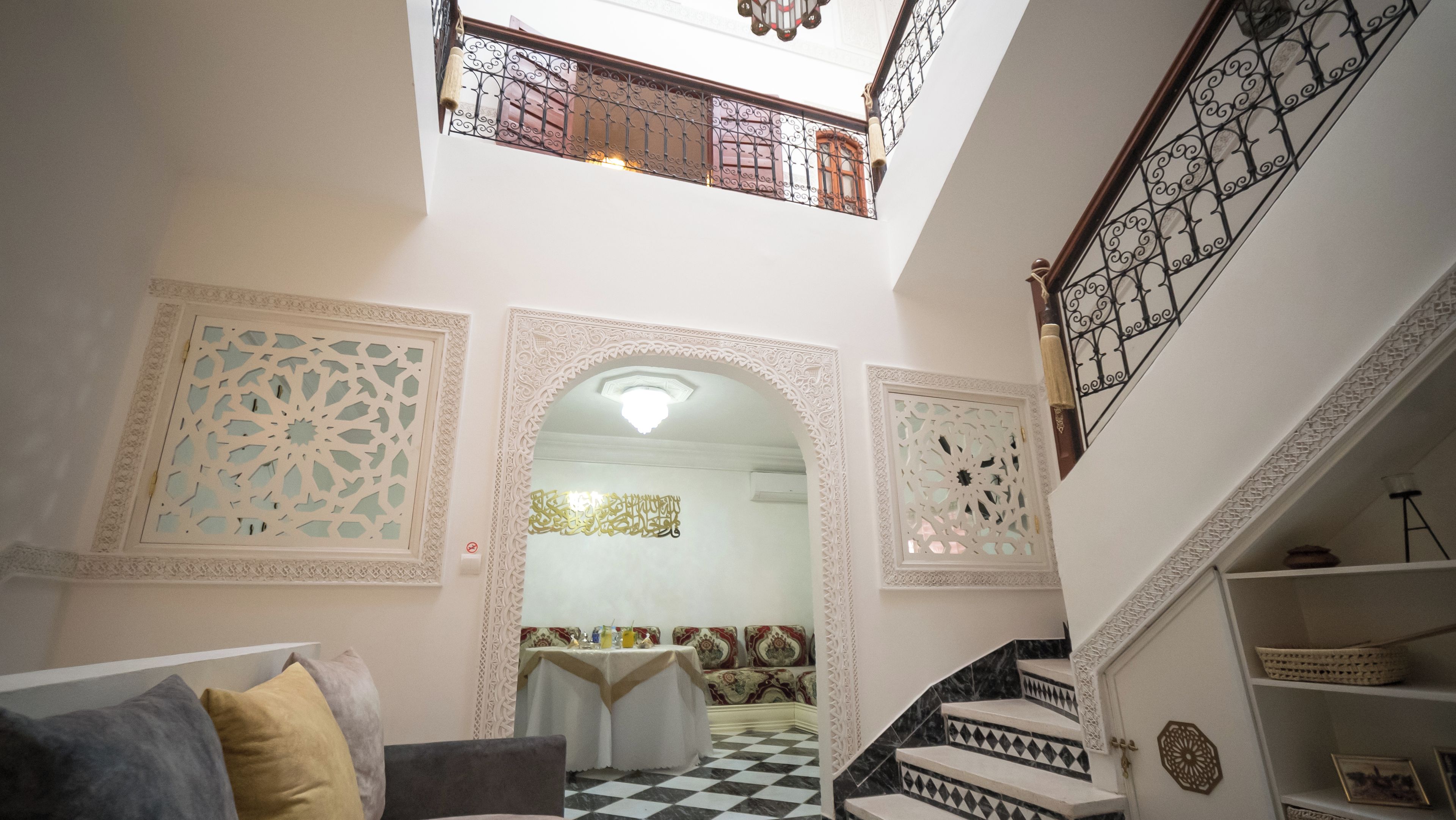 A multi-level interior with ornate architectural details, a staircase with patterned railings, and a checkered floor.