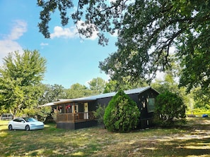 A small cabin with a deck, surrounded by trees and a parked car. - Bass & Jellyfish Retreat 3BR, 2BA Sleeps More with Flexible 4-Bedroom Setup (Athens)
