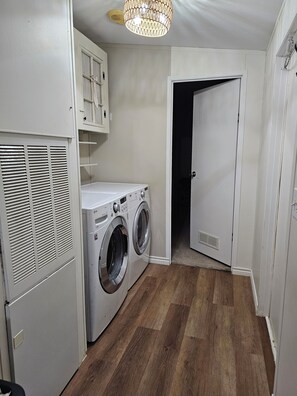 A laundry room with a washing machine and dryer, a ceiling fan, and a door leading to another room. - Bass & Jellyfish Retreat 3BR, 2BA Sleeps More with Flexible 4-Bedroom Setup (Athens)