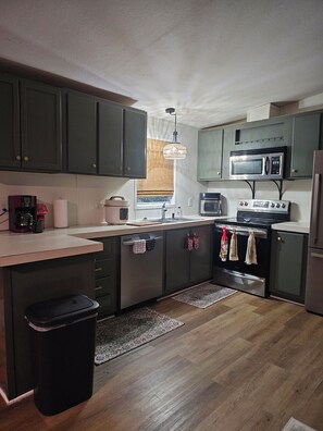 A kitchen with dark cabinets, a microwave, an oven, a sink, and a trash bin. - Bass & Jellyfish Retreat 3BR, 2BA Sleeps More with Flexible 4-Bedroom Setup (Athens)