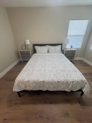 A bedroom with a large bed, two bedside tables, and a window with blinds. - The Valley Haus (Sanger)