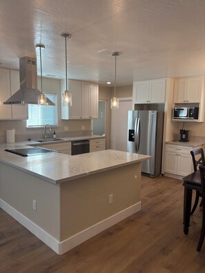 A modern kitchen with a central island, stainless steel appliances, pendant lighting, and white cabinetry. - The Valley Haus (Sanger)