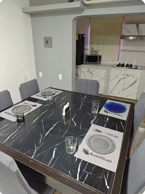 A dining area with a marble table, grey chairs, and a kitchen in the background. - New Listing (Guadalupe)