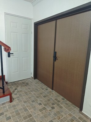 A hallway with a white door and a brown sliding door. A wooden staircase with a black handrail is visible on the left. The floor is tiled with a patterned design. - New Listing (Guadalupe)