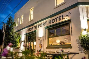 Exterior de l'Hotel North Port, amb un rètol sobre l'entrada, una finestra visible i una taula amb caires a l'exterior.