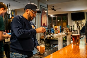 A bartender pouring a drink from a tap into a glass.