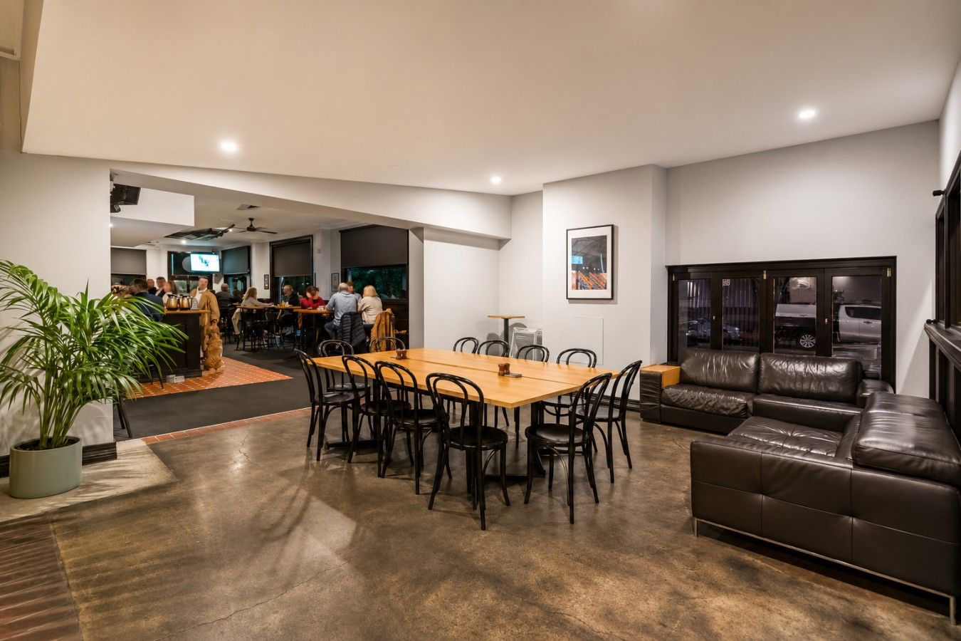 A spacious living area with a dining table, leather sofa, and a potted plant.