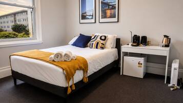 Una habitación de hotel con cama, escritorio, cafetera y refrigerador pequeño.