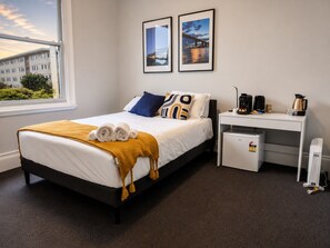 A hotel room with a bed, a desk, a coffee maker, and a mini fridge.