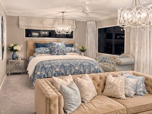 A bedroom with a large bed, a sofa, a chandelier, and a ceiling fan. - Palms on Tindalls Beach side retreat (Whangaparāoa)