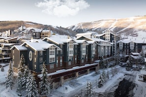Un hôtel à plusieurs étages doté d’un atrium central, entouré d’arbres couverts de neige et avec une chaîne de montagnes en toile de fond.