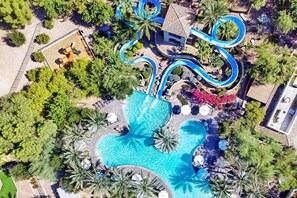 Luftaufnahme eines Resorts mit einem großen Schwimmbad, einer Wasserrutsche und Palmen.