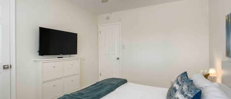 Un dormitorio con una cama, un ventilador de techo, un televisor sobre un mueble y una puerta.