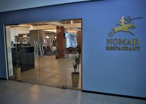 The entrance to a restaurant with a glass door and a logo featuring a running figure. - Optima Almaty (Almaty)
