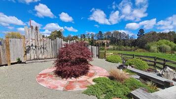 A gravel patio with a red circular area, a wooden fence, and a small bush.