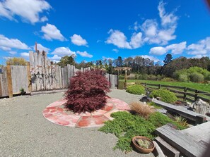 Un patio de grava con una zona circular roja, una valla de madera y un pequeño arbusto.