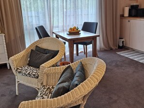 Una habitación con un sofá de mimbre, una mesa de comedor con un frutero y una cocina con cafetera.