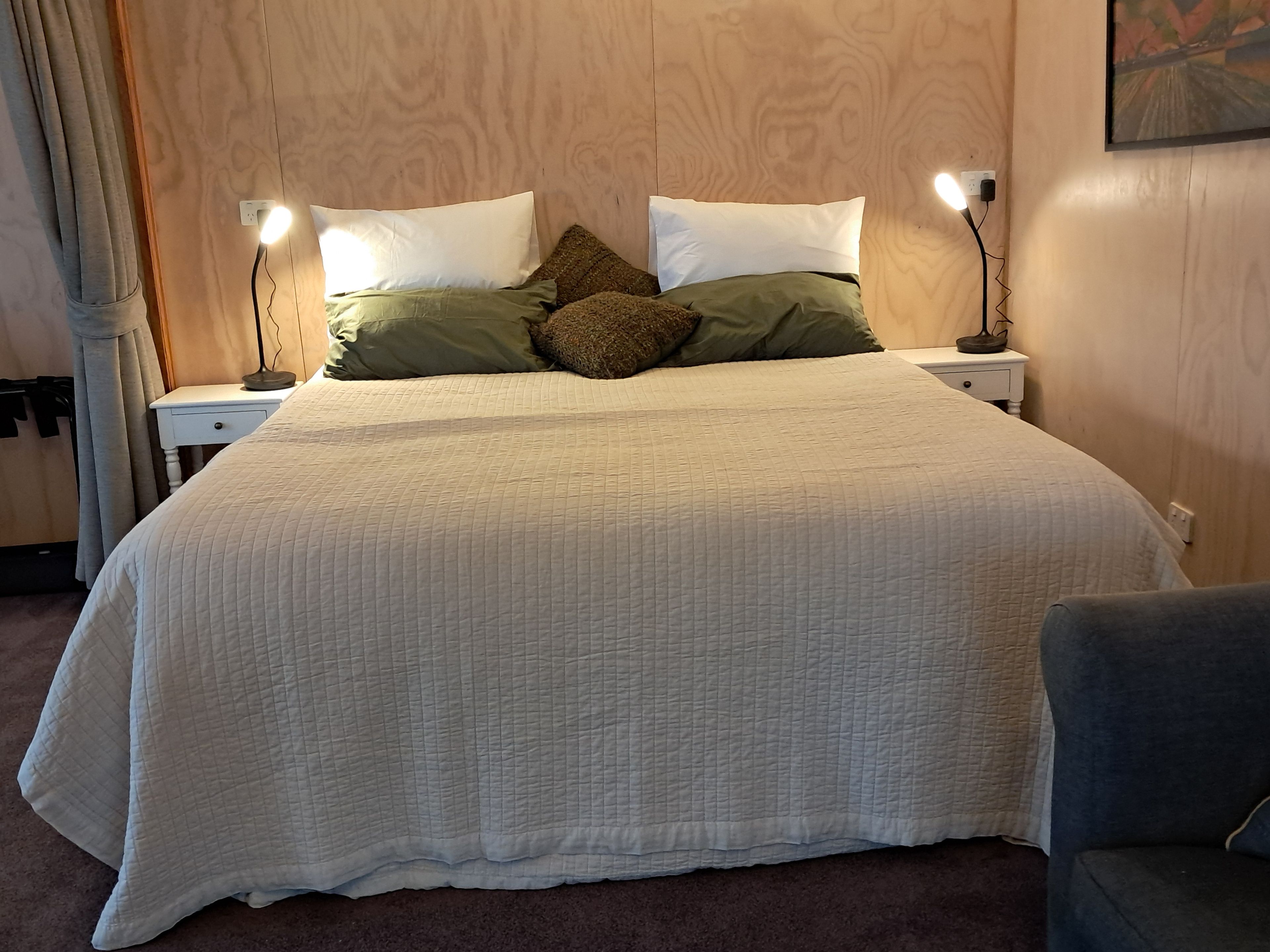 A neatly made bed with a quilted white duvet, two bedside lamps, and a nightstand with a lamp.