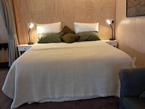 Una cama bien tendida con edredón blanco acolchado, dos lámparas de noche y una mesita con lámpara.