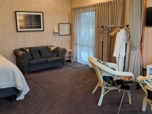 Una habitación de hotel con sofá, una silla, una mesa, perchero y cama.