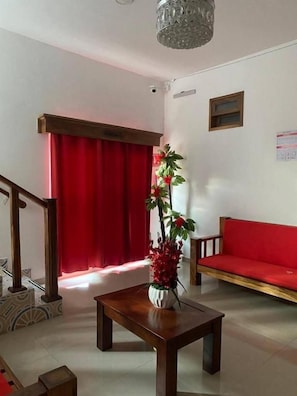 Een kamer met een houten tafel, een rode bank, een rood gordijn en een plant.