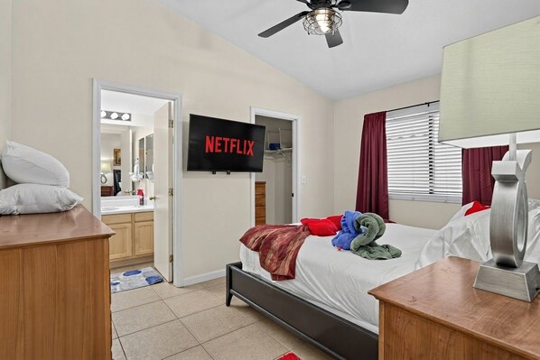Una habitación de hotel con una cama, televisor montado en la pared, ventilador de techo y mesita de noche.