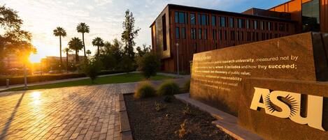 A university campus with a modern building, a paved walkway, and a sign with the university's name.