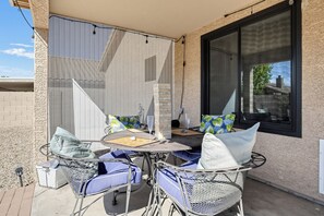 Un patio exterior con una mesa redonda y sillas, una ventana con persianas y una pared de ladrillo.
