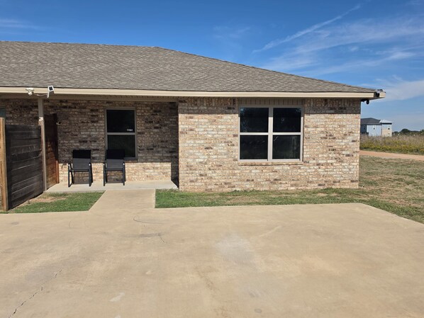A single-story house with a brick exterior, a garage door, and a small porch with two chairs.
