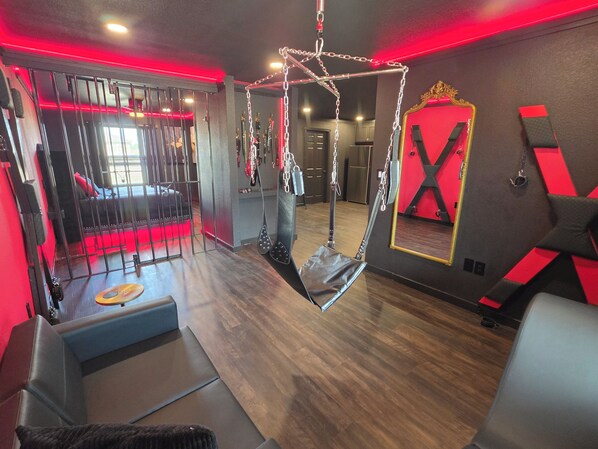 A room with a hanging chair, a mirror, and a red-lit wall.