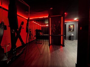 A room with a red-lit bar area, a black sofa, and a tripod in the foreground. - Adult Only - SPICY King Bed. Clean. Couples retreat. (Thackerville)