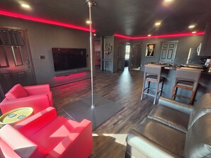 A modern living room with a flat-screen TV, red and black furniture, and a kitchen area with a bar.