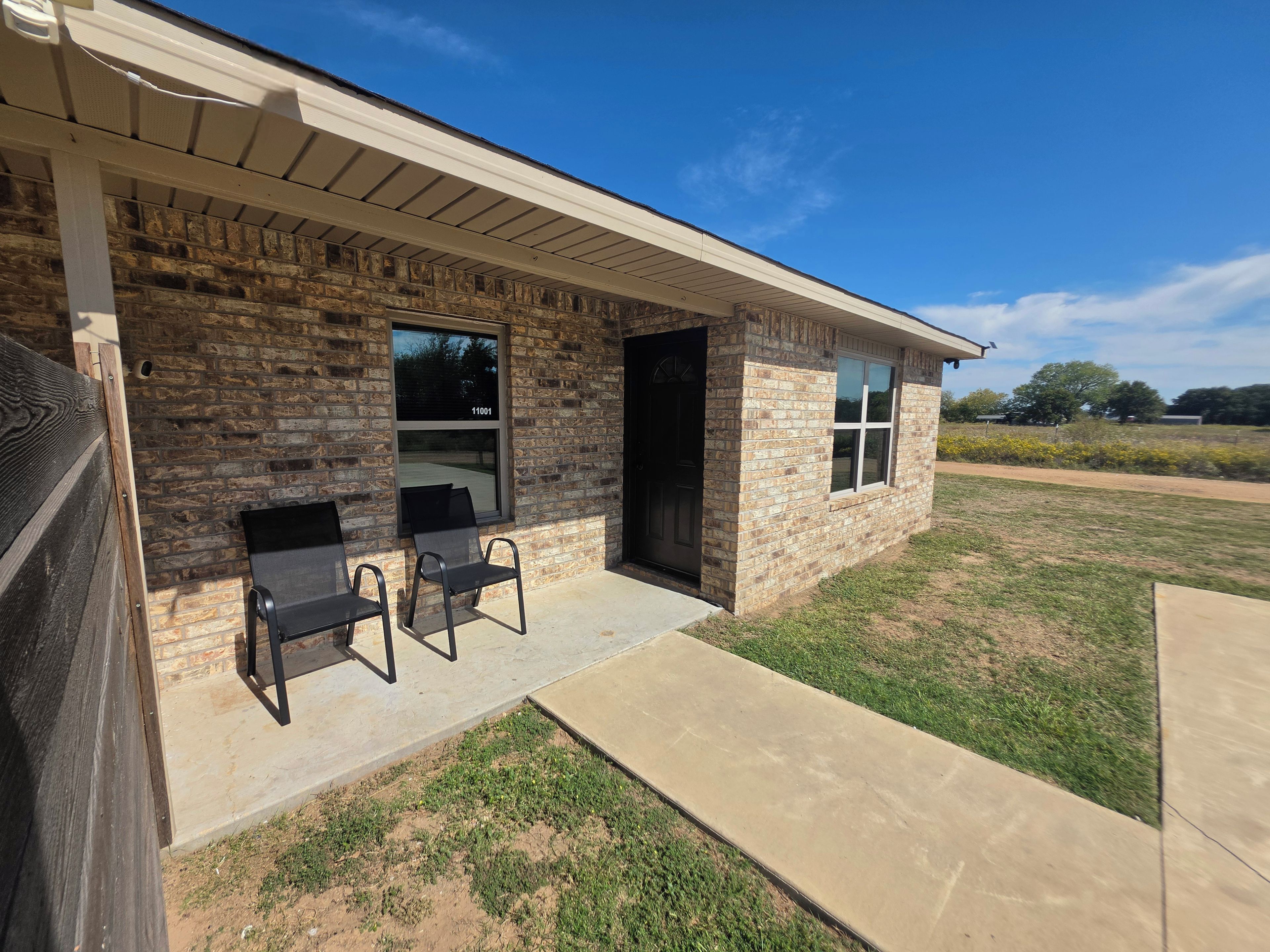 A single-story brick building with a covered porch, two chairs, and a clear sky.