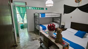 A room with bunk beds, a desk with a chair, a hanging light fixture, and a door leading to another room.