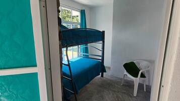 Una habitación con literas, una pequeña silla blanca y una ventana con cortinas.