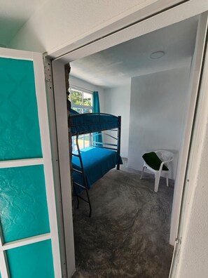 Una habitación con literas, una pequeña silla blanca y una ventana con cortinas.