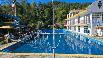 A swimming pool with a metal safety barrier, surrounded by a grassy area and a building with balconies.